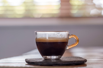 Cup of espresso coffee in front of window with blinds
