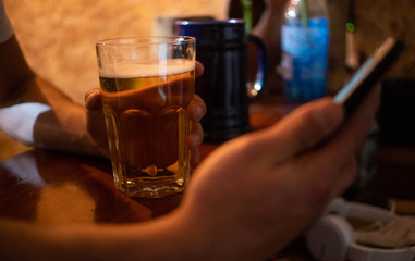 Closeup of man with beer bottle using phone at bar