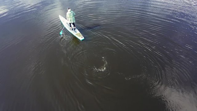 Aerial view of young person in jacket training on a SUP board on a river in sunny day. Footage. Concept of water tourism, healthy lifestyle and recreation