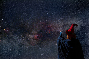 A woman in a red hat is watching the night sky. She sees the Milky Way with many stars. Concept:...