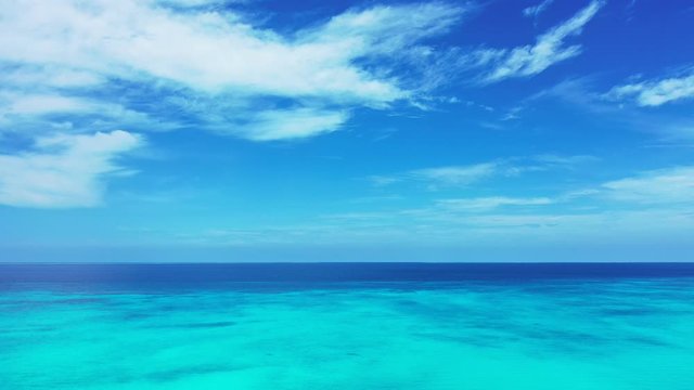 Paradise tropical seascape with white clouds on bright sky over navy blue ocean and turquoise lagoon in Caribbean, copy space