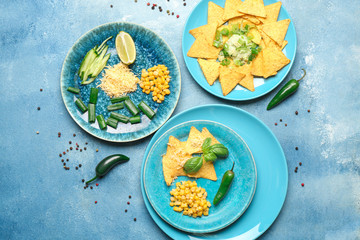 Plates with tasty nachos, corn, and cheese on color background