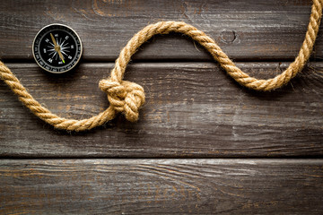 Goal achievement concept. Compass near rope with knot on dar wooden background top view copy space