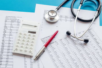 Health insurance concept. Stethoscope near financial documents and calculator on blue background