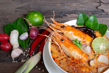Tom Yum Goong or Shrimp soup spicy sour Soup Traditional food in Thailand contains chili, lime,lemongrass, lime leaf, along with cooked rice in a white dish on the old wood background from top view.