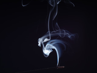 Abstract swirl of white smoke from smouldering incense stick, isolated on black background, close up view. Structure of smoke, brush effect. Eastern fragrance for meditation and relaxation