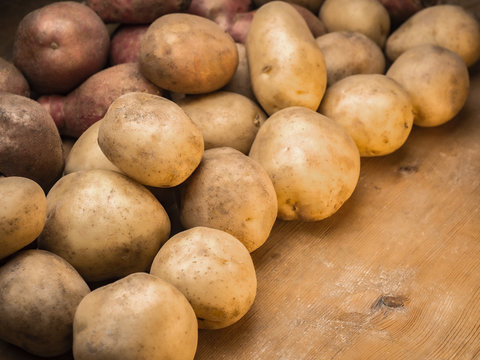 Rustic environmentally friendly potatoes. Vegetables from farmhouse field is lying in bulk on wooden table from planks. Place for your text in one corner of picture. The image is shot at angle.