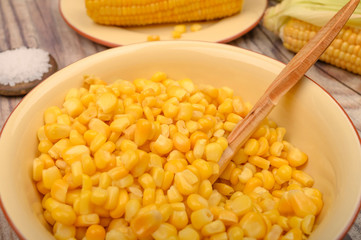 Grains of sweet corn in a plate with a wooden spoon and ears of corn on the table. Healthy diet. Fitness diet. For a sweet treat. Close up.