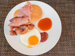 Hotel breakfast with egg, pancakes, bacon and ham on plate
