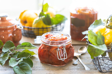Homemade quince jam in a glass jar on an old wooden background. Fresh fruits and leaves of eggs...