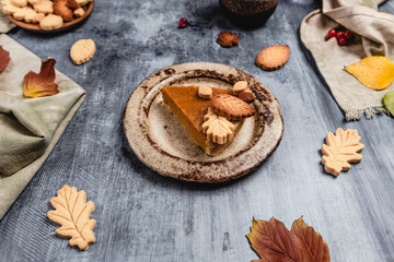 Obraz na płótnie Canvas traditional pumpkin pie decorated with leaves shaped cookies on shabby blue background with coffee and textile