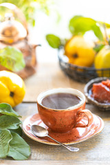 Cup of tea with homemade quince jam on an old wooden background. Fresh fruits and quince leaves on the background.