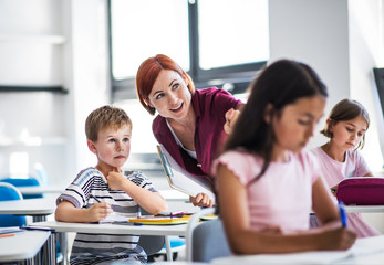 A teacher walking among small school children on the lesson, explaining.