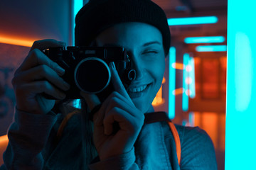 Smiling female photographer using camera in neon light - obrazy, fototapety, plakaty
