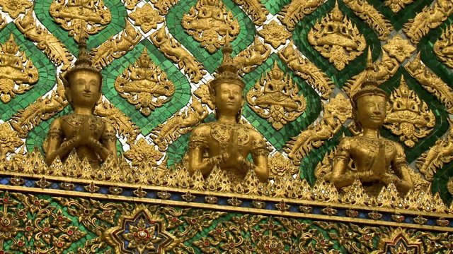 A steady closeup shot of the fa ade and roof cornice detailing of the Phra Mondop of Wat Si Rattana Satadaram, with golden Buddha sculptures and foliage ornamentation accompanied by vibrant mosaic and