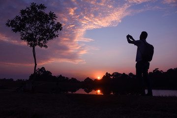 Photographer taking pictures outdoors, silhouette of a man with camera over sunset