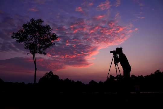 Photographer taking pictures outdoors, silhouette of a woman with camera over sunset