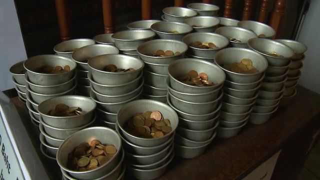 A daylight closeup shot of a stack of metal bowls containing coin offerings to be dropped in the bronze jars at Wat Pho temple in Thailand.
