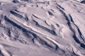 Fototapeta premium The surface of the snow cover in the light of the sun, with abstract patterns formed by the wind, a copy space, close-up, toned.