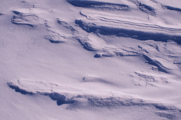 Fototapeta premium The surface of the snow cover in the light of the sun, with abstract patterns formed by the wind, a copy space, close-up, toned.