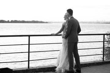 Young beautiful couple of newlyweds with bride and groom walk on the terrace by the ocean during a wedding ceremony in a wedding dress and suit kissing and hugging. Love and lovestory.