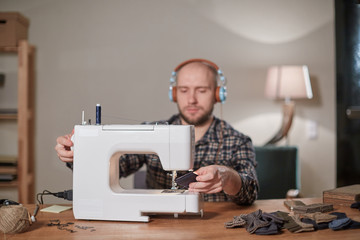 Man listen music and working with sewing machine in a textile studio. Tailor makes bow ties of woolen fabric.