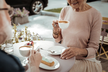 Joyful aged woman drinking her tasty cappuccino