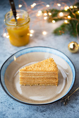 A piece of delicious honey cake lies in a plate with festive garlands in the background. Vertical orientation. Selective focus.