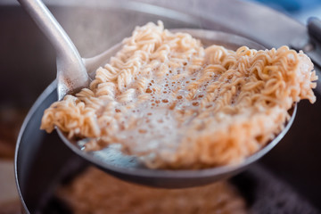 Instant noodles were blanched in a boiling hot water pot and being scooped up using a dipper.