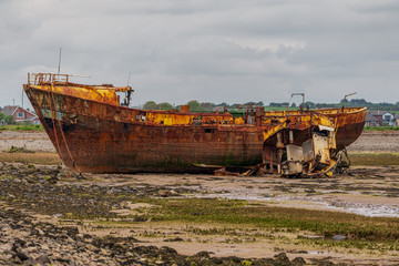 A rusty shipwreck in the mud of the Walney Channel, seen from the road to Roa Island, Cumbria,...