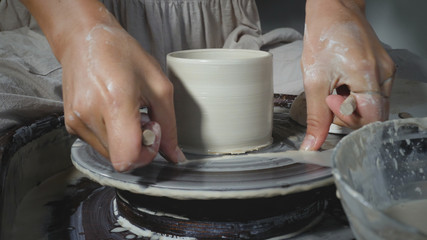 Close-up of female potter cuts clay pot from pottery wheel with special thread. Professional female potter working in workshop. Concept of small pottery business