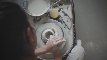 Top down shot of dark haired female master potter molds clay pot at pottery wheel. Woman works in pottery workshop © Azhorov