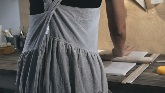 Master female potter wearing an apron preparing and rolling clay with a rollingpin. Female hands rolling out raw clay with wooden rolling pin - Powered by Adobe