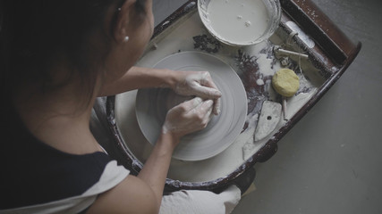 Over shoulder shot of master female potter creating ceramic pot on spinning potters's wheel. Female potter works in studio. Traditional pottery concept