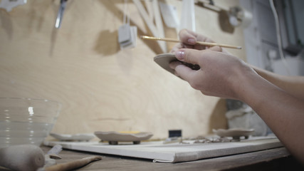 Close-up of female potter cover raw clay product with water using brush. Professional potter putting a water to the detail by brush. Female potter work in her studio