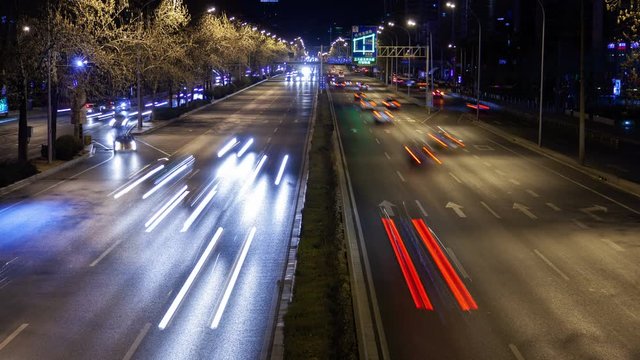 Timelapse wide Chinese multi-lane street highway with driving cars at bright illumination between trees in Beijing city district at dark night