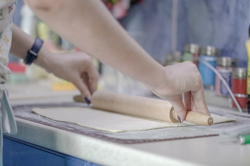 Woman rolls puff pastry with a wooden rolling pin on a silicone Mat for dough. The process of cooking baking.