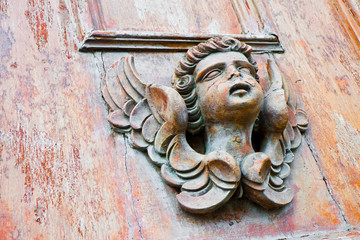 Sculpture of an old wooden angel against a wooden door of a church - more than 100 years old