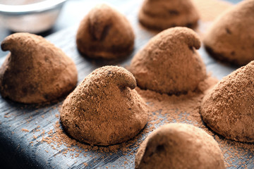 Delicious chocolate truffles sprinkled with cocoa powder and walnuts on a wooden stand. Dark concrete background.