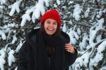 portrait of young smiling woman in winter clothes in red hat with bubo fir tree in background