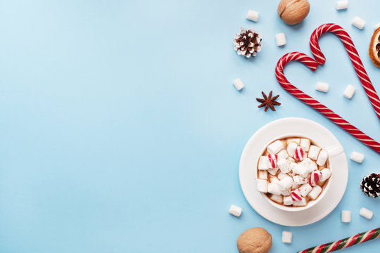 Cup of hot chocolate with marshmallow cocoa powder and caramel nuts, oranges on pastel blue background with copy space. Christmas winter concept.