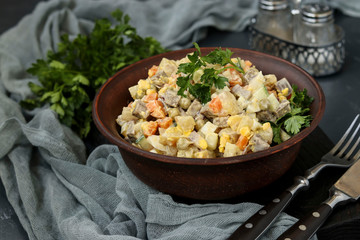 Traditional Russian festive salad Olivier with tongue in a bowl against a dark background, horizontal orientation