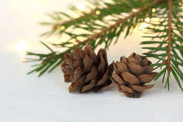 Fototapeta premium two cones and a fir branch on a background of blurry lights close-up. atmosphere of winter holidays