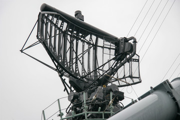 The radar system on a warship against a gray sky. A lot of cables and metal parts. Rainy gloomy weather.