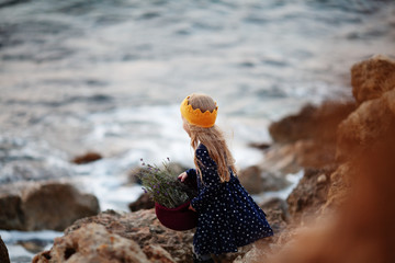 Fototapeta na wymiar A pretty girl in a yellow knitted crown holds a basket of cord in her hands and stands on the seashore