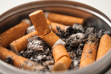 Closeup of metallic ashtray full of cigarettes habits on white background