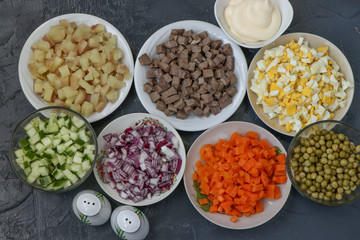 Ingredients for the preparation of Olivier salad: beef tongue, cucumbers, red onions, potatoes, carrots, eggs, canned peas and mayonnaise, top view