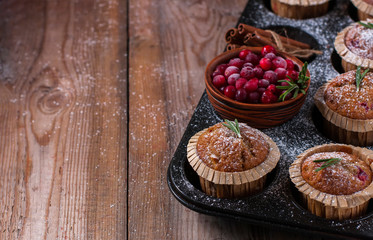 Fresh homemade Cranberry muffins in baking form on wooden table with Christmas decoration. Muffins in eco-friendly recyclable paper packaging. Selective focus, copy space.