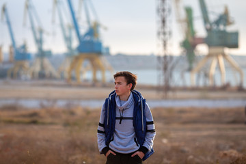 Naklejka premium Portrait of a handsome serious brutal guy. Teenager stands on the background of cranes