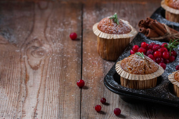 Fresh homemade Cranberry muffins in baking form on wooden table with Christmas decoration. Muffins in eco-friendly recyclable paper packaging. Selective focus, copy space.